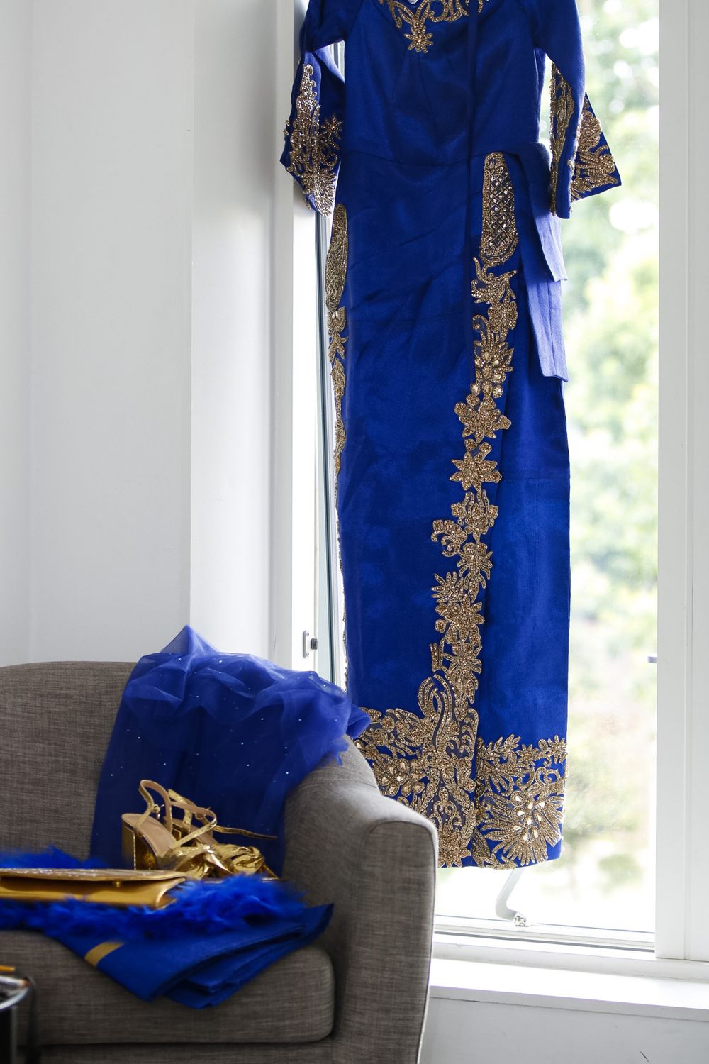 Royal blue traditional dress with gold embroidery details displayed near a window.