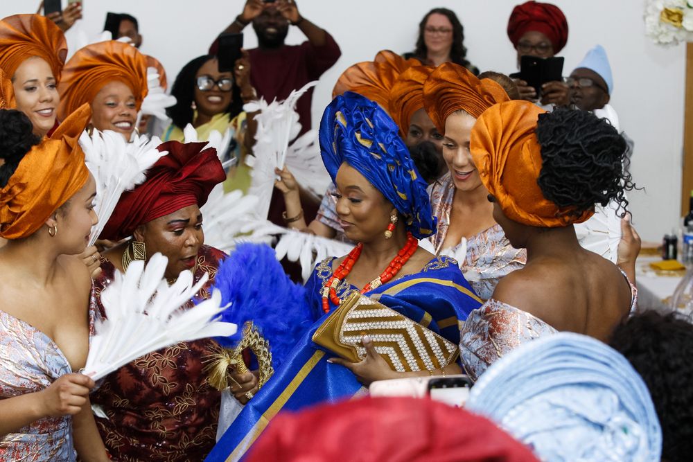 A celebratory gathering shows people in vibrant orange and blue traditional African attire.