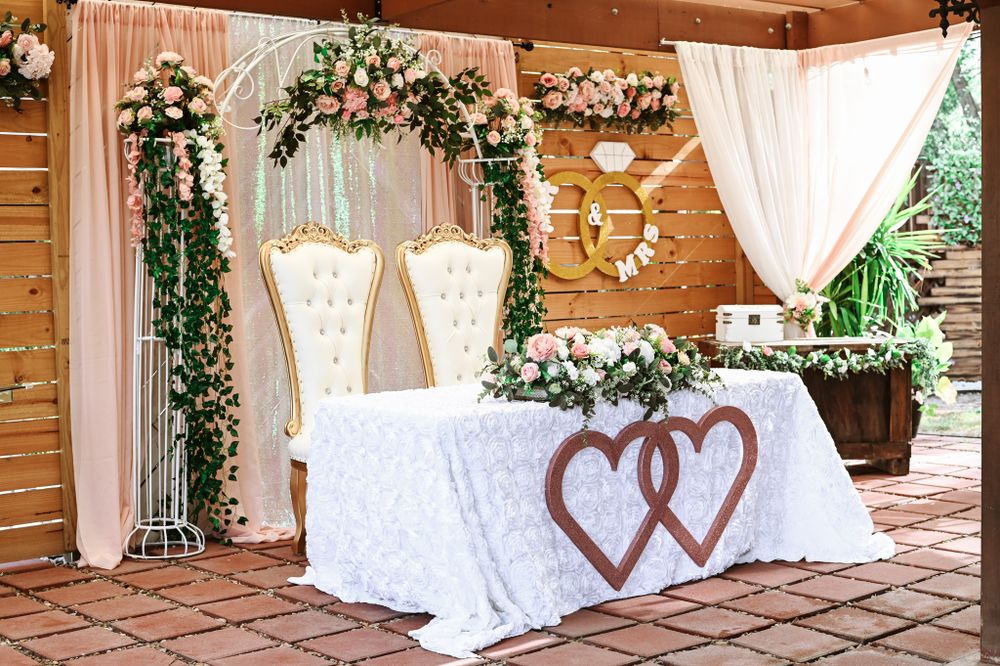 Romantic wedding ceremony setup with white chairs, floral arch and heart-decorated sweetheart table.