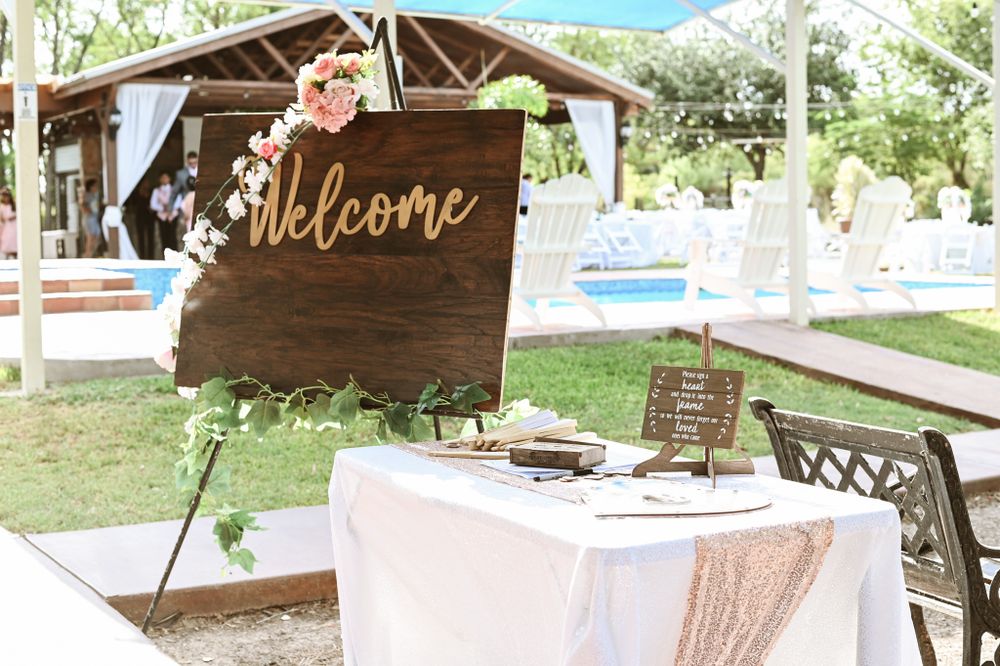 Rustic wooden welcome sign and guest book table with white linens at outdoor wedding venue.