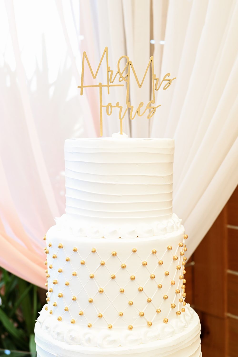 Elegant white wedding cake with gold heart details and a gold 'Mr and Mrs' cake topper.