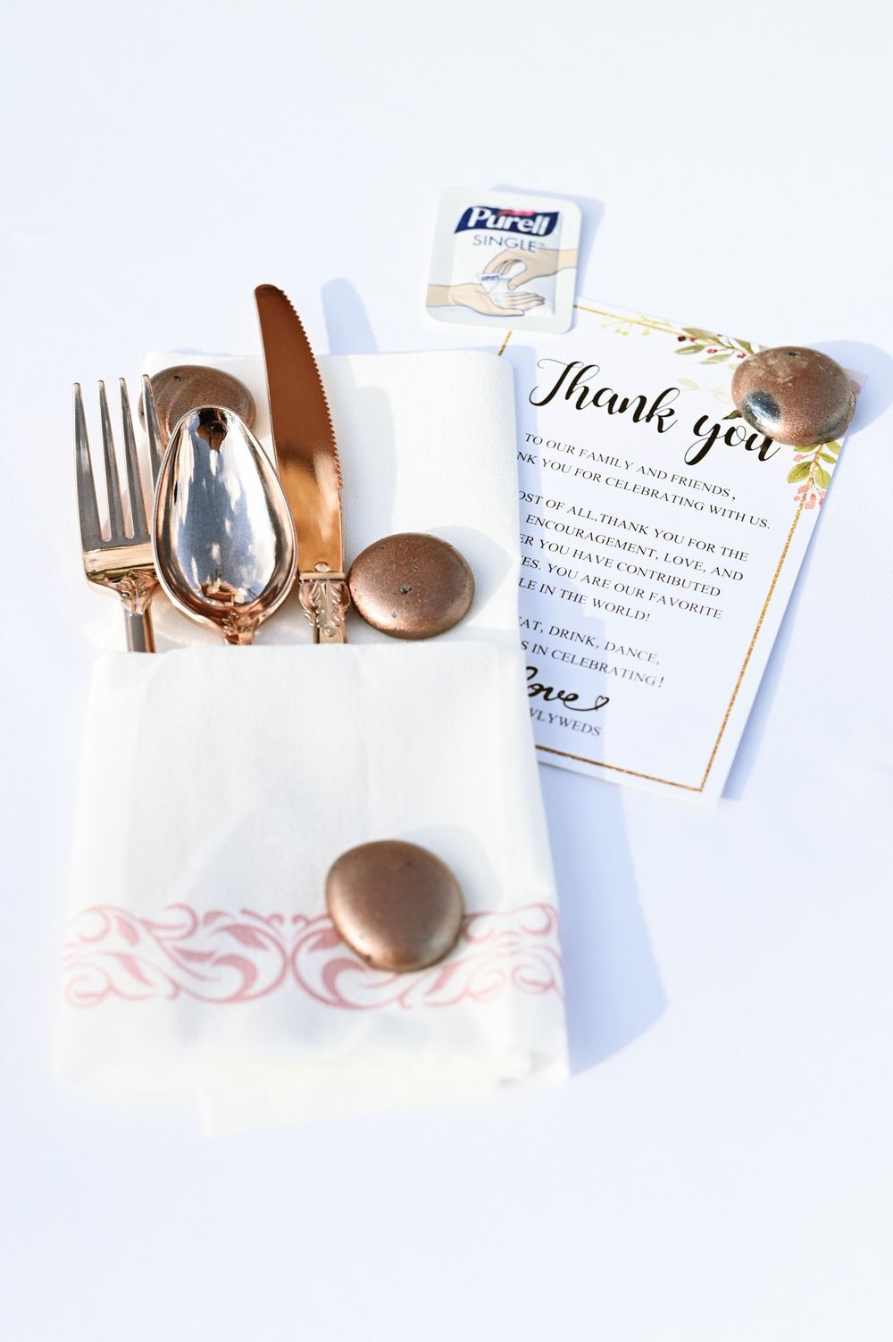 Place setting with gold cutlery, napkin, and thank you note at a wedding reception.