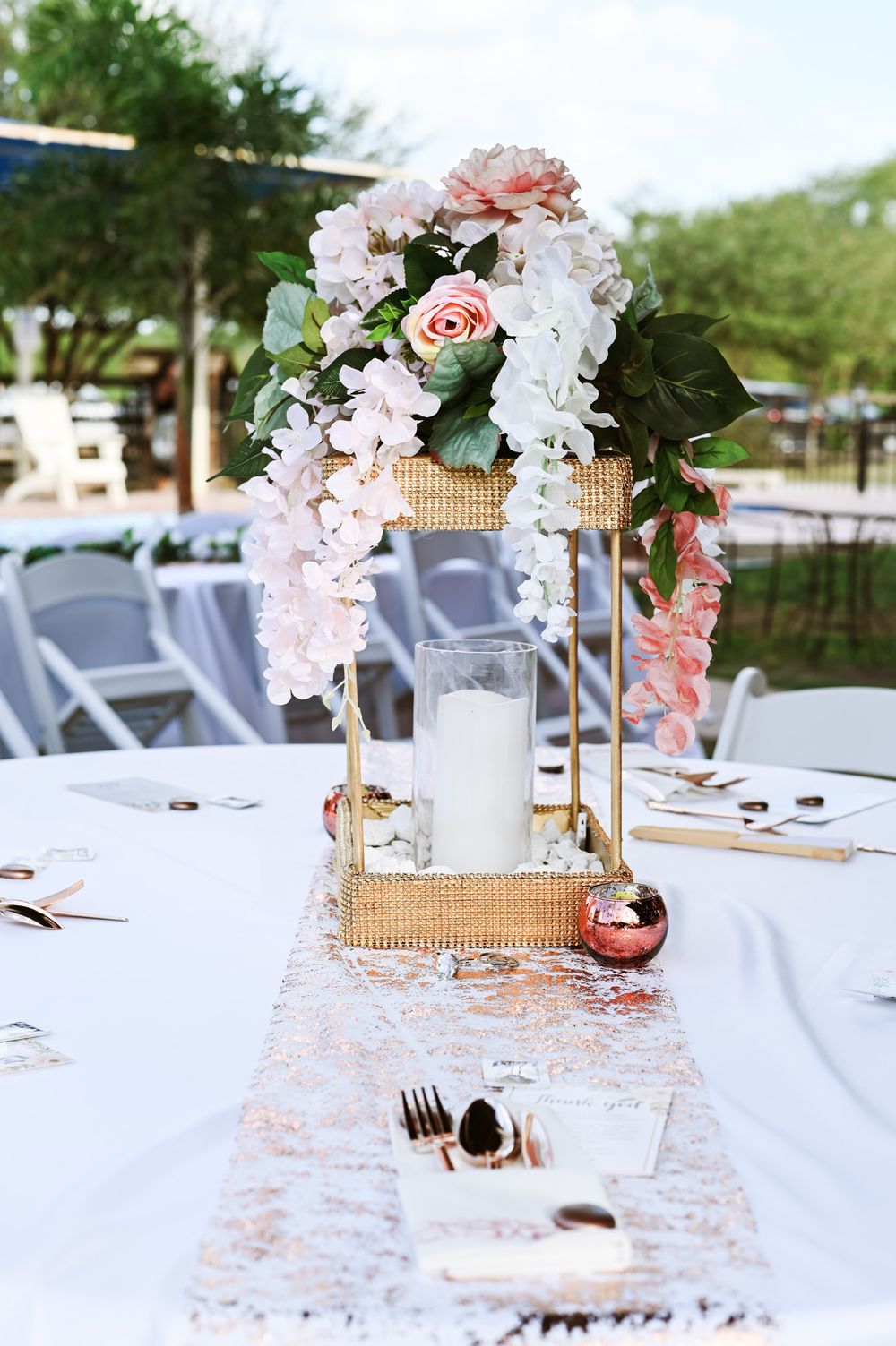 Elegant wedding table centerpiece with pink flowers and gold lantern on white tablecloth.