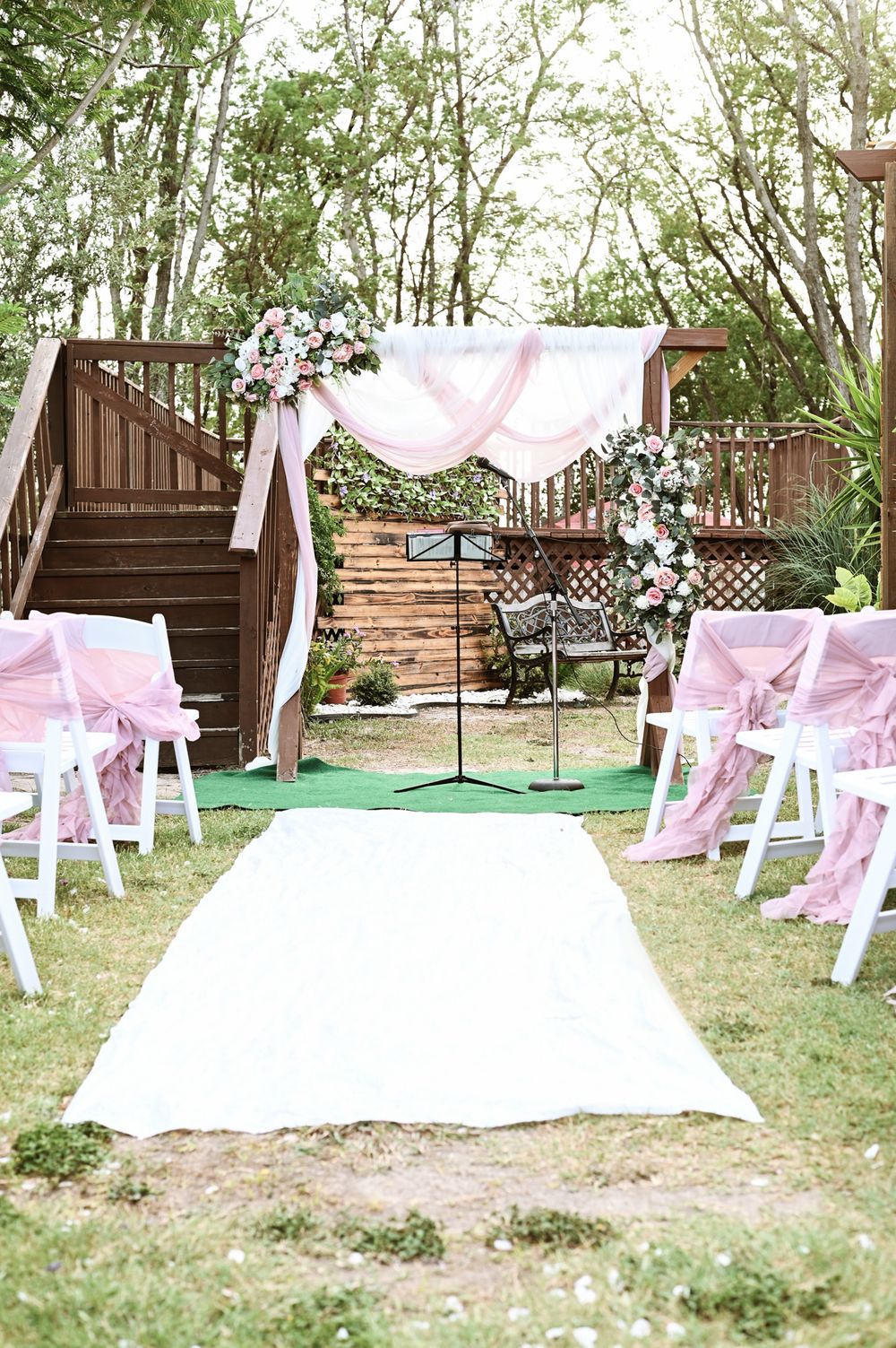 Outdoor wedding ceremony setup with white aisle runner and pink fabric decorations.