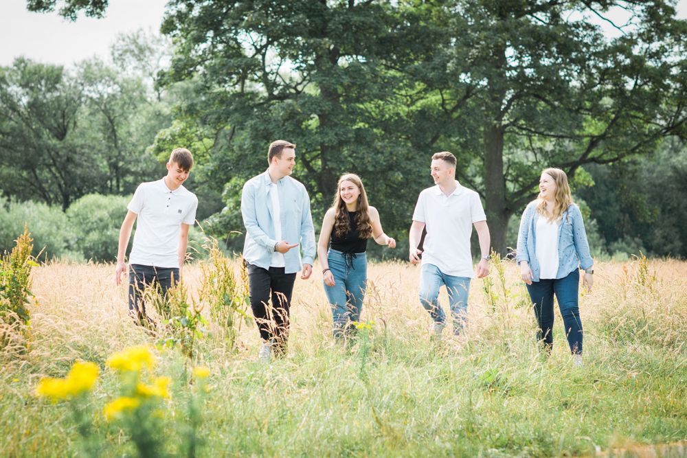 Five teenage cousins walking through long grass together in the sunshine.
