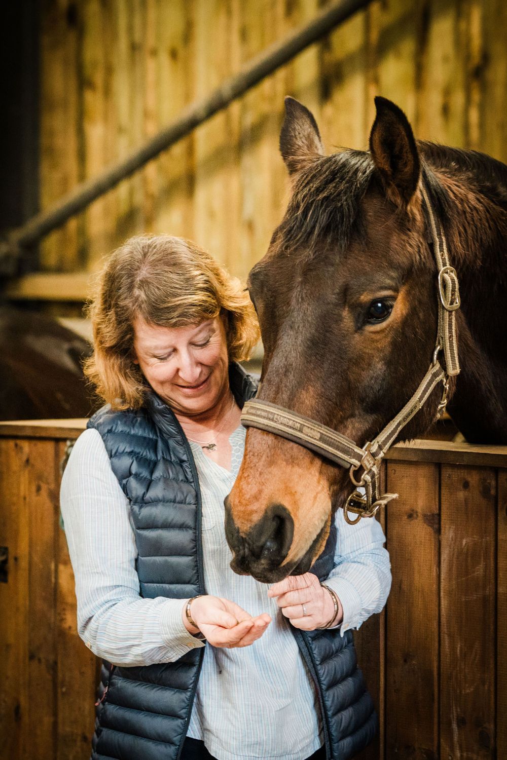 A portrait of a lady smiling while feeding her horse.