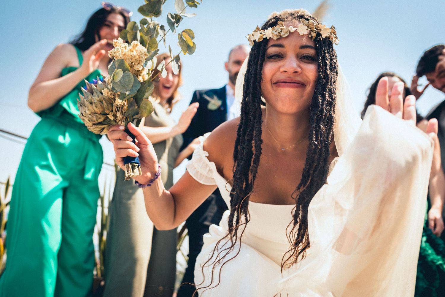 Wedding party celebrates joyfully outdoors with bridesmaids in emerald green dresses and groomsmen in dark suits.
