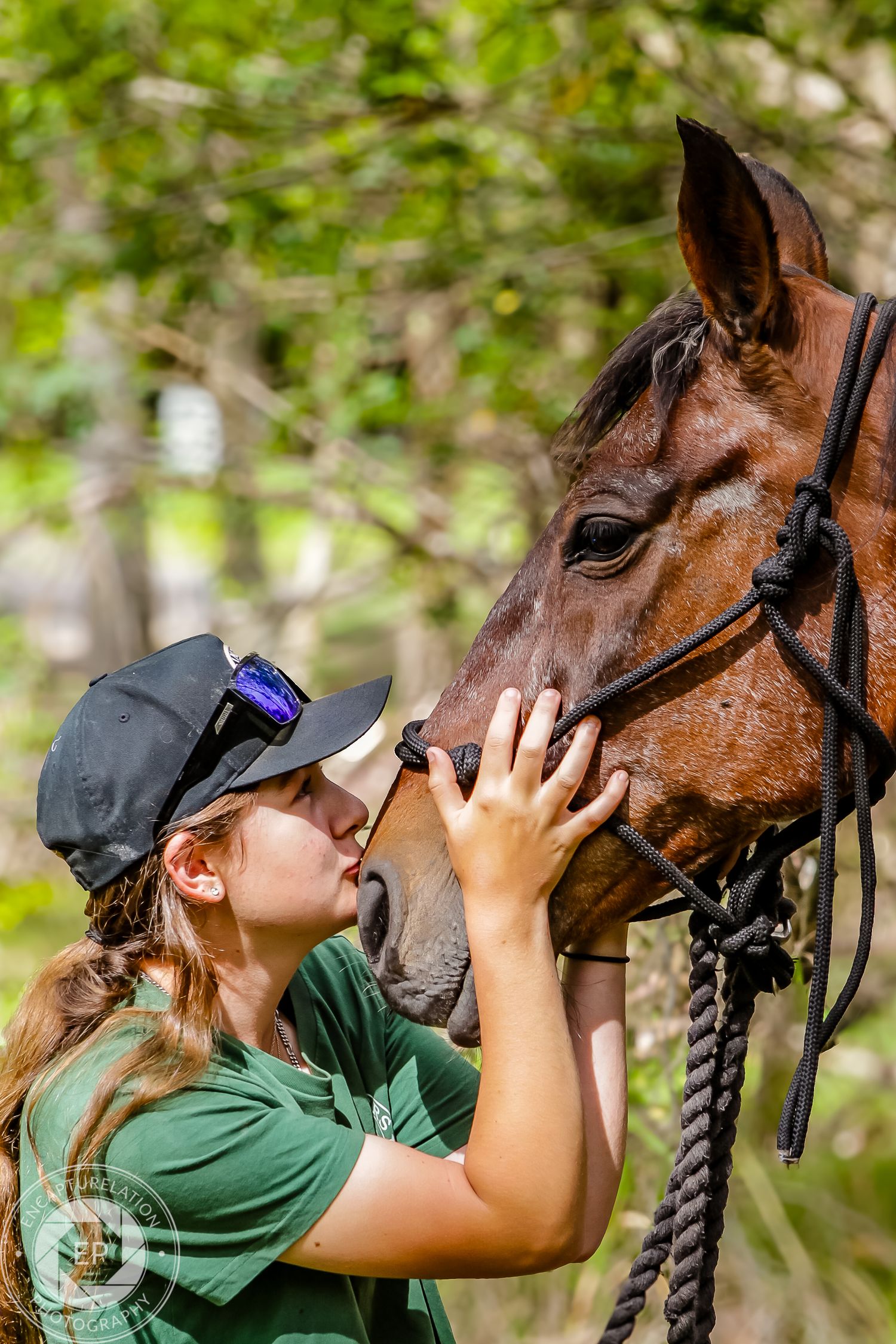 A person in a green shirt gives affection to a brown horse wearing a bridle.