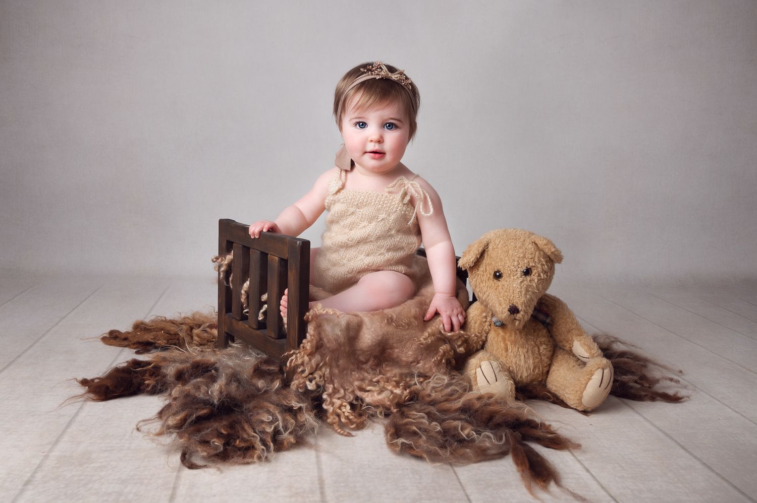 Baby portrait with wooden crate and plush dog toy on fur rug.