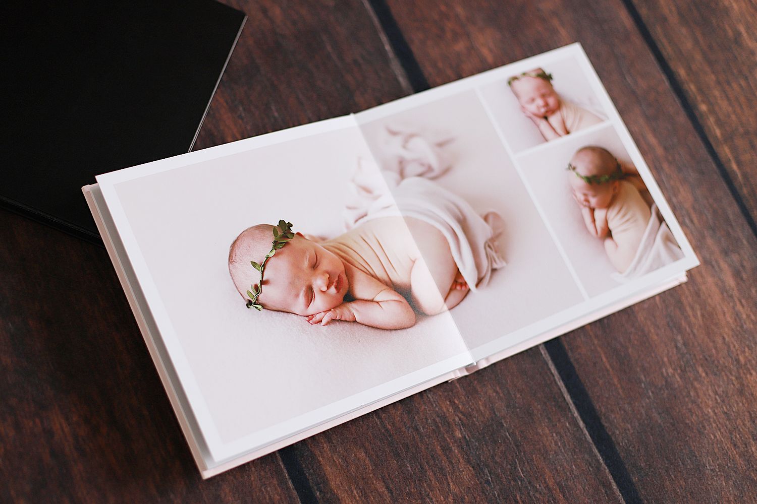 White photo album displaying newborn portraits on wooden table.