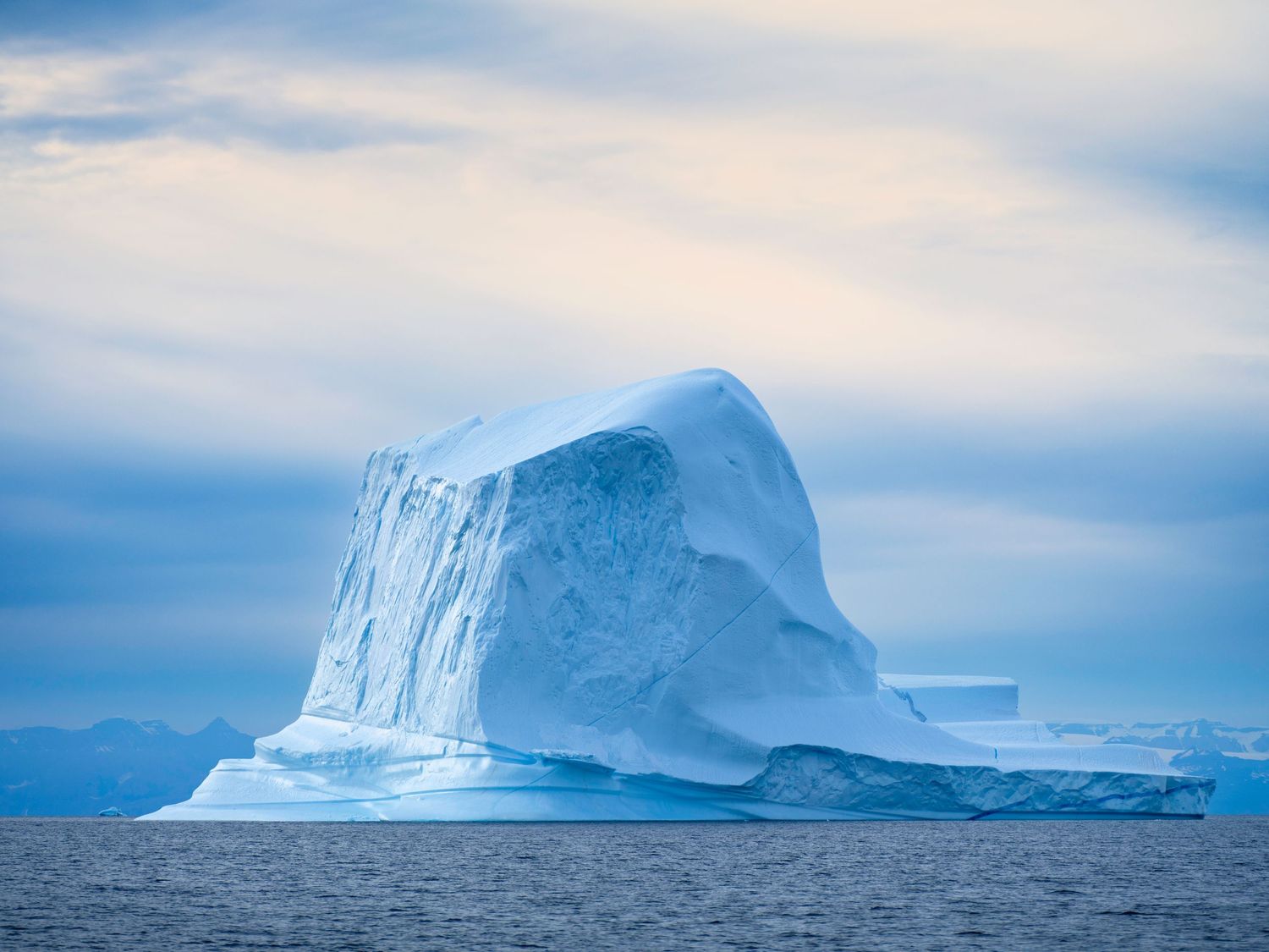 Massive blue iceberg floating in ocean under cloudy arctic sky.