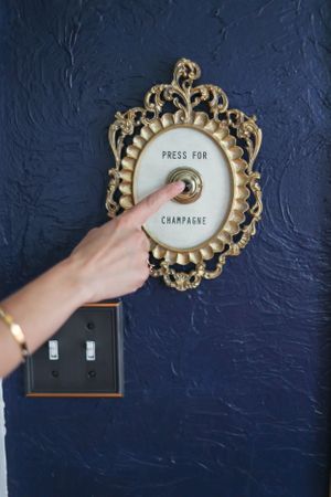Decorative gold frame being mounted on navy blue textured wall with 'Press for Champagne' text.