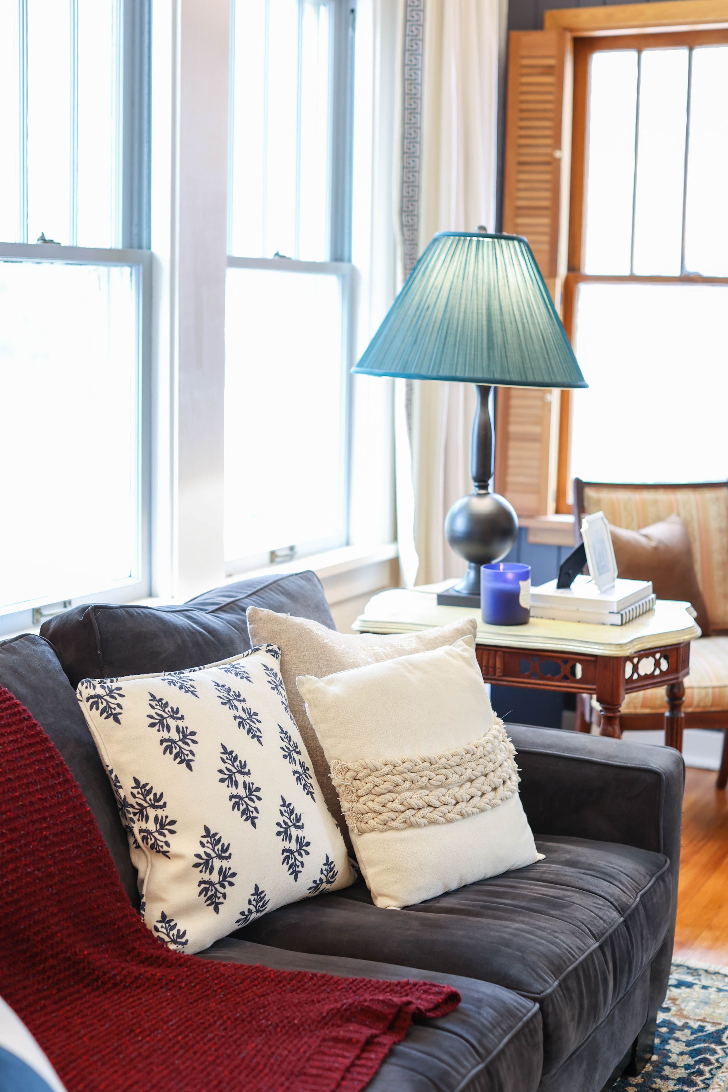 Cozy seating area with navy sofa, decorative pillows, and table lamp near bright windows.