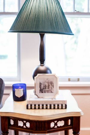 Side table with green pleated lampshade and decorative objects in natural lighting.