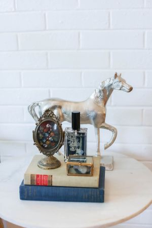 Vintage-inspired vignette with white horse figurine, antique books, and decorative clock on white surface.