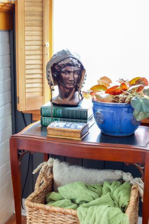 Wooden side table with blue bowl of fruit and decorative accessories near window shutters.