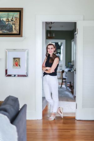 A gray cat sits in a doorway of a bright home interior with hardwood floors and white walls.