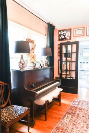 Piano room with dark furniture, hardwood floors, and an oriental rug in warm lighting.