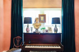 Digital piano setup against emerald curtains with crown molding and peach-colored walls.