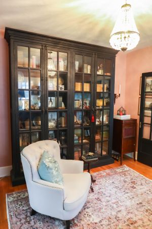 Elegant sitting area with white accent chairs, built-in dark cabinets, and a pink floral area rug.