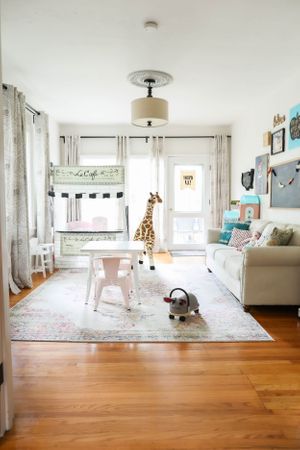 Airy playroom with white furniture, hardwood floors, and sheer curtains letting in natural light.