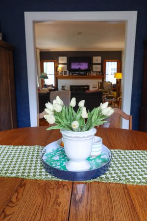 White tulips in ceramic bowl on green patterned table runner.