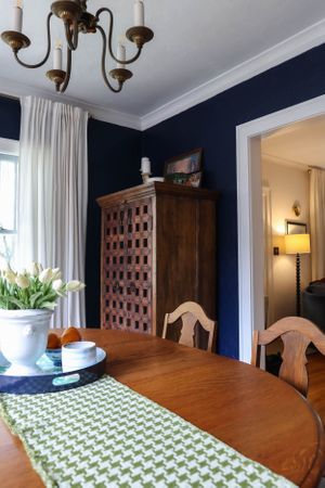 Dining room with chandelier, navy walls, and green patterned table runner.