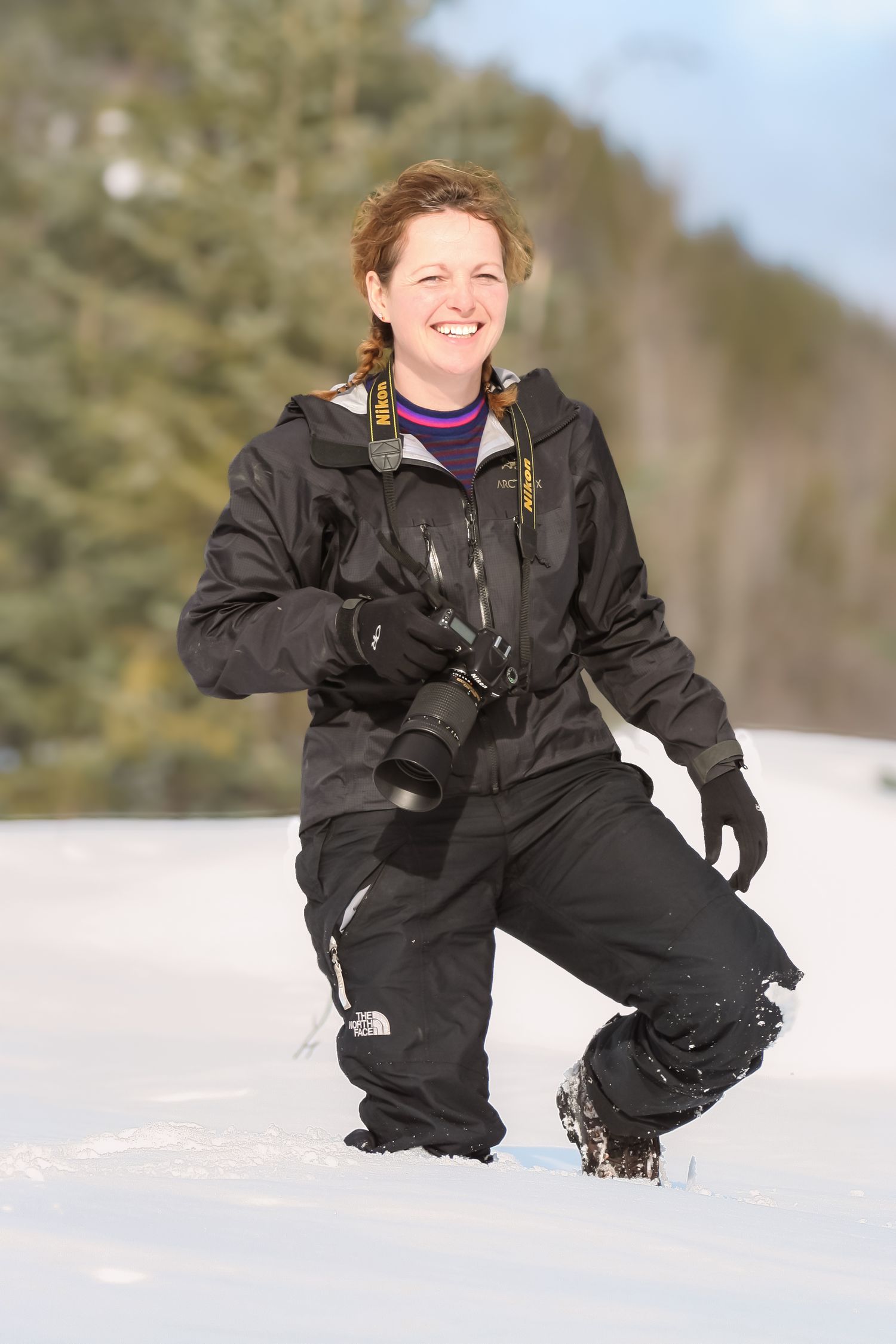 Person in black winter gear kneeling in deep snow on sunny winter day.
