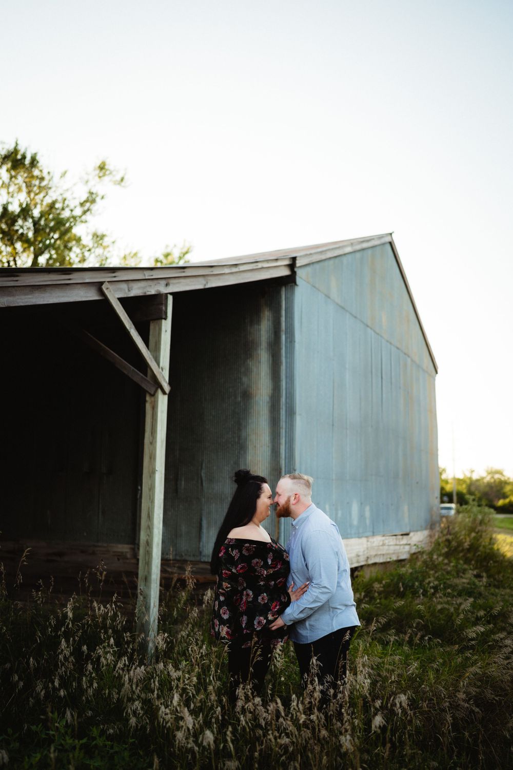A couple sharing an intimate moment beside a rustic barn at sunset.