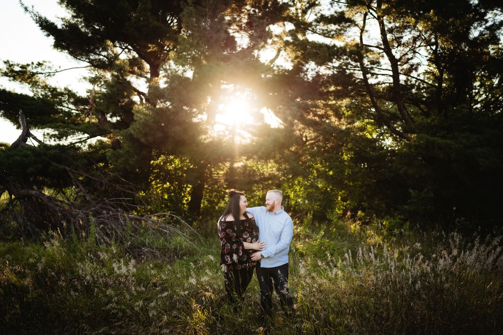 Silhouette of two people standing together in a field at sunset with trees in the background.
