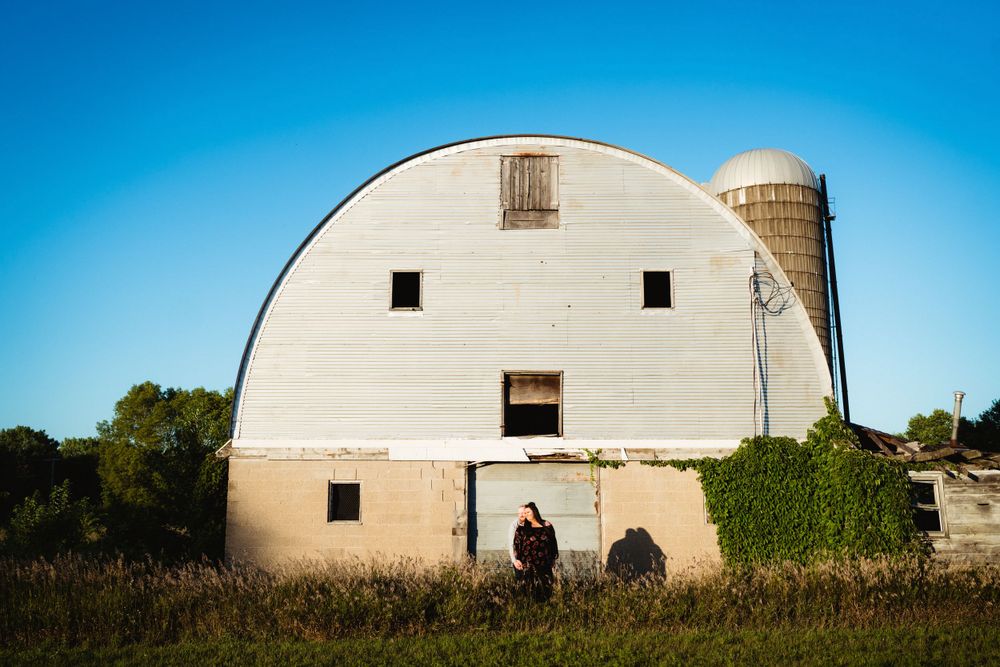A classic white rounded-roof barn with silo against bright blue sky.