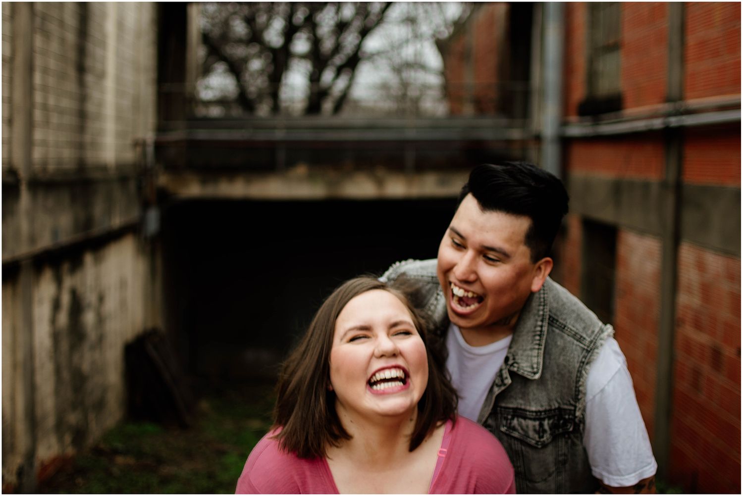 Candid moment of laughter shared between couple against industrial brick backdrop.