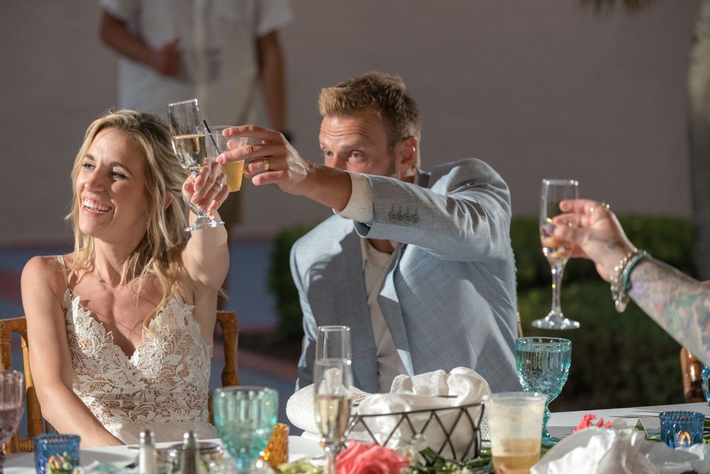 Wedding party toasting with champagne glasses at reception table.
