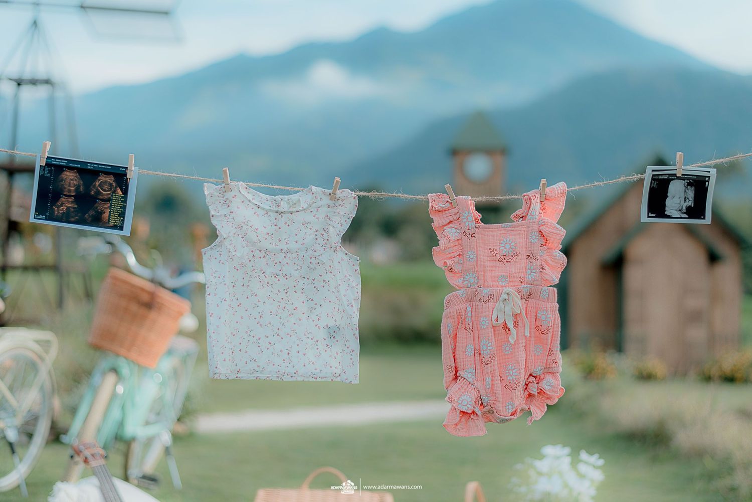 Baby clothes hanging on clothesline with mountain landscape in background.