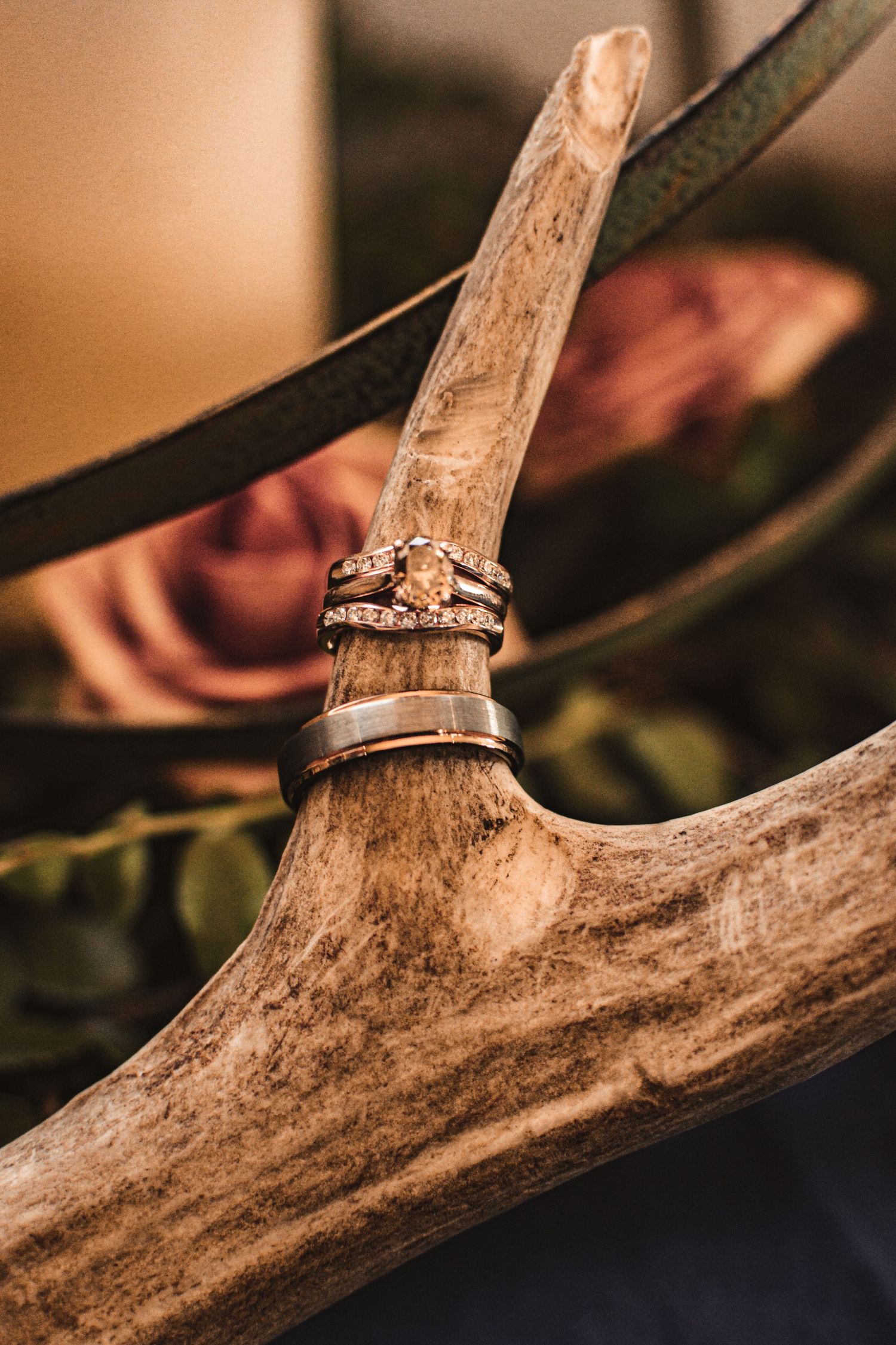 Wedding rings artistically displayed on antler with soft pink floral background.