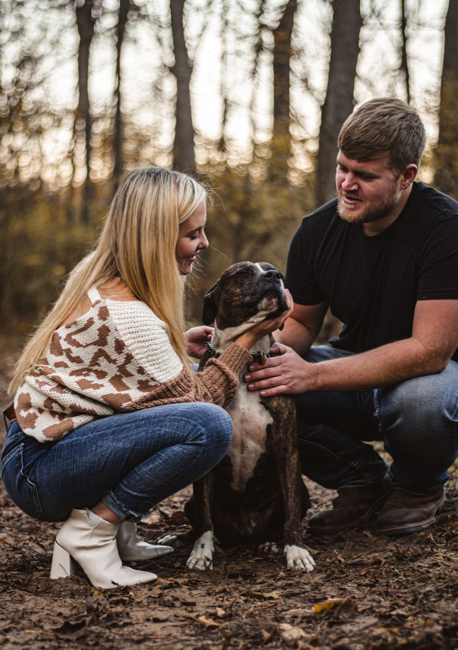 Couple plays with their pit bull mix dog in autumn forest setting.