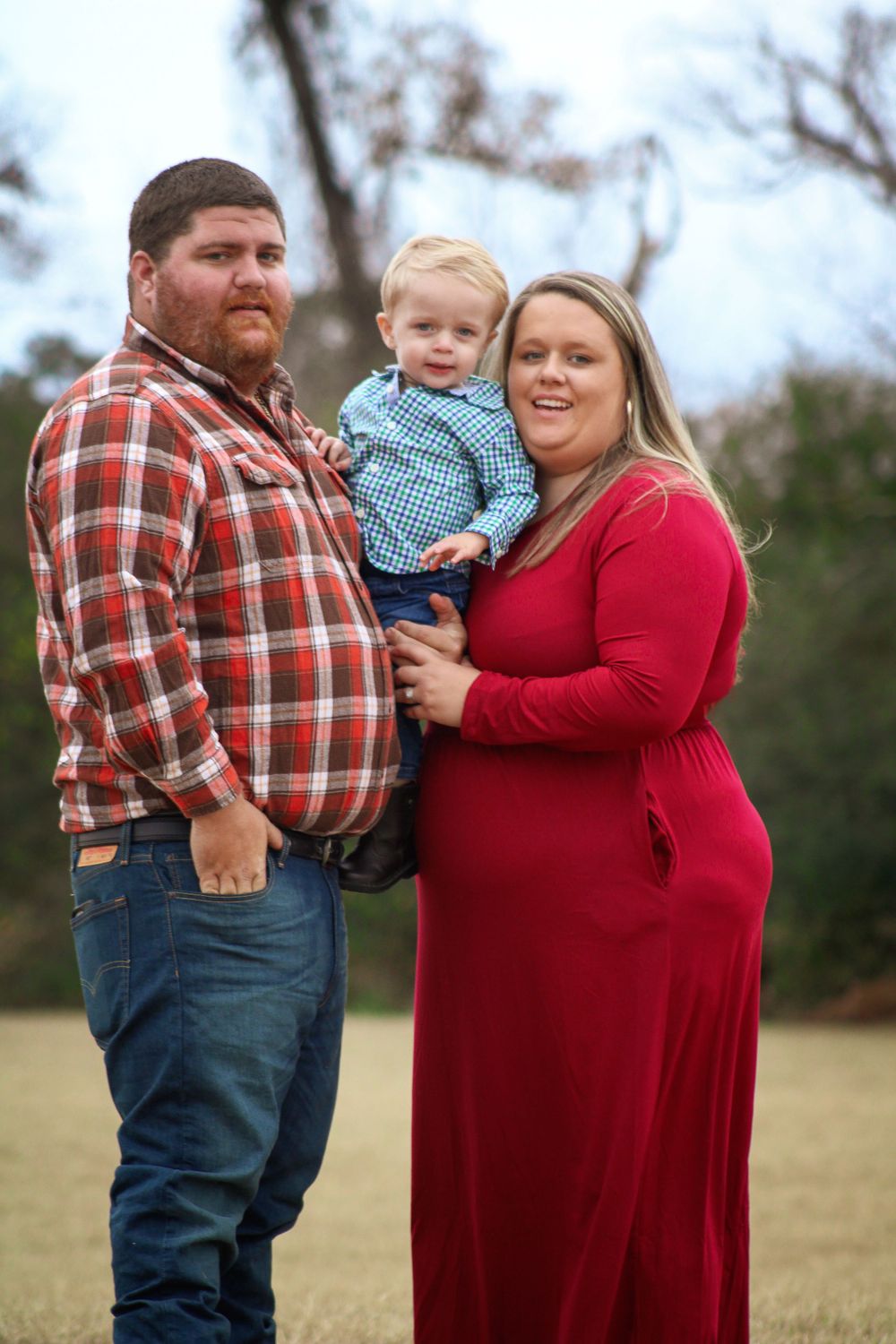 Family of three poses together outdoors in casual country attire.