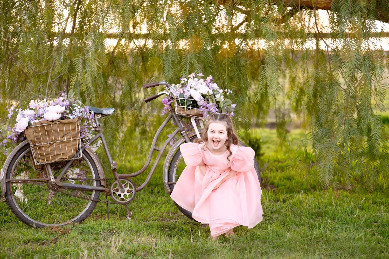 Vintage bicycle decorated with flowers next to someone in a pink dress in a garden setting.