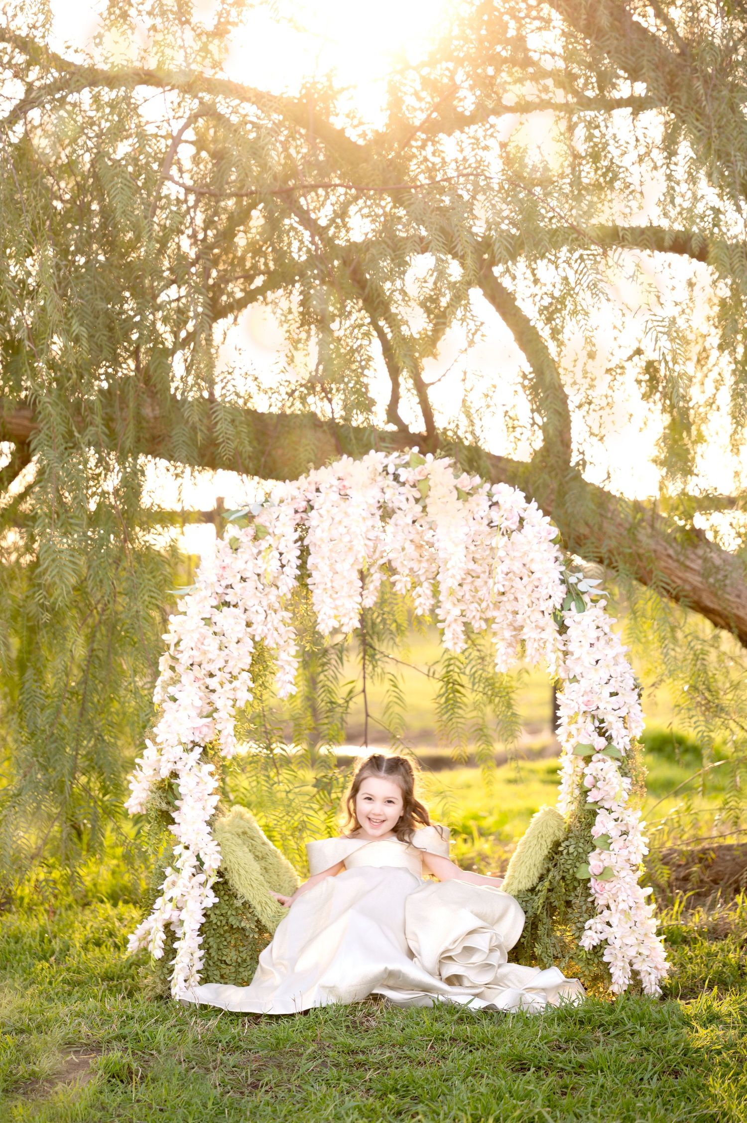 Enchanting garden scene with white floral arch and willow trees at golden hour.