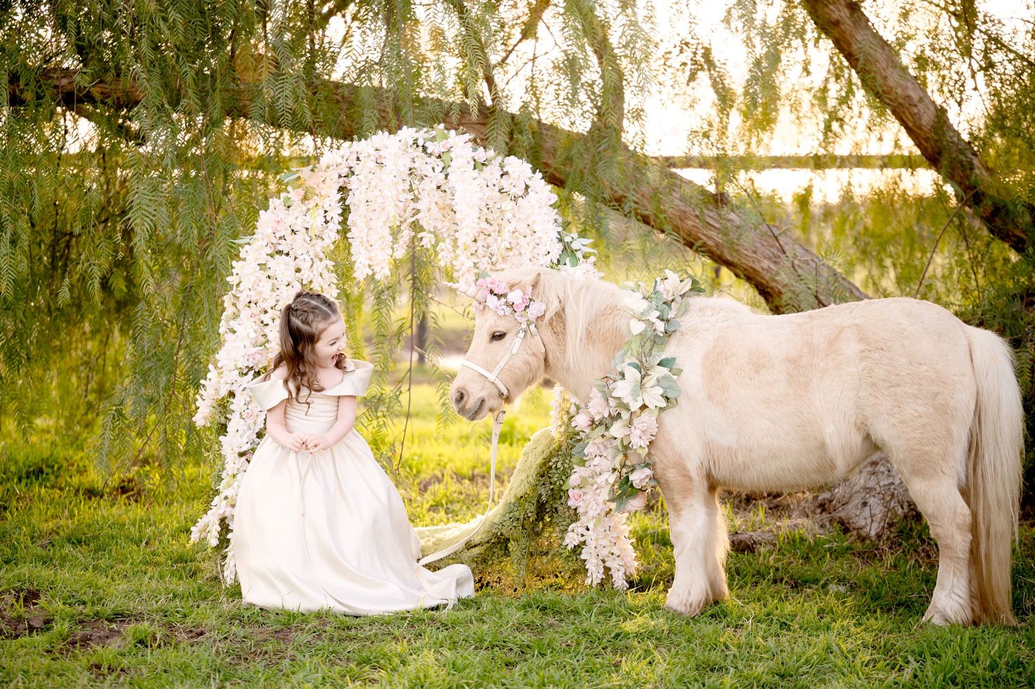 Ethereal garden scene with white unicorn and floral decorations under willow trees.