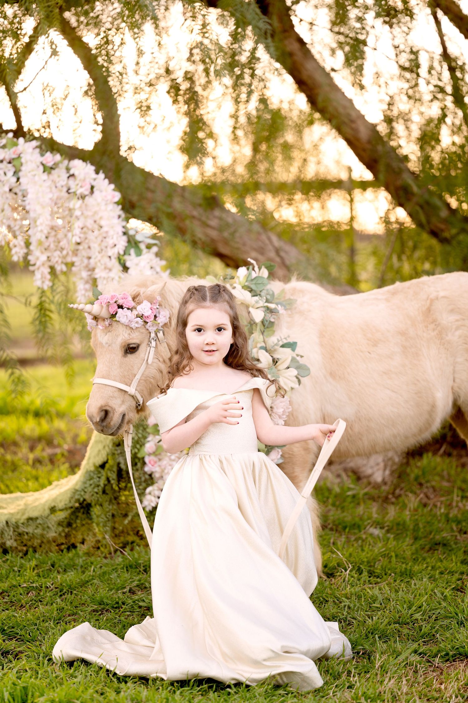 Enchanted garden portrait with cream-colored pony and blooming cherry blossoms.