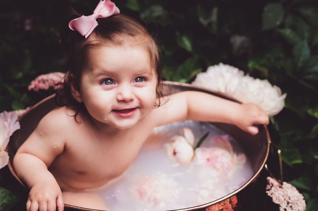 7-month-old baby girl grips the sides of a copper tub filled with milky water and peonies for milk bath session outside