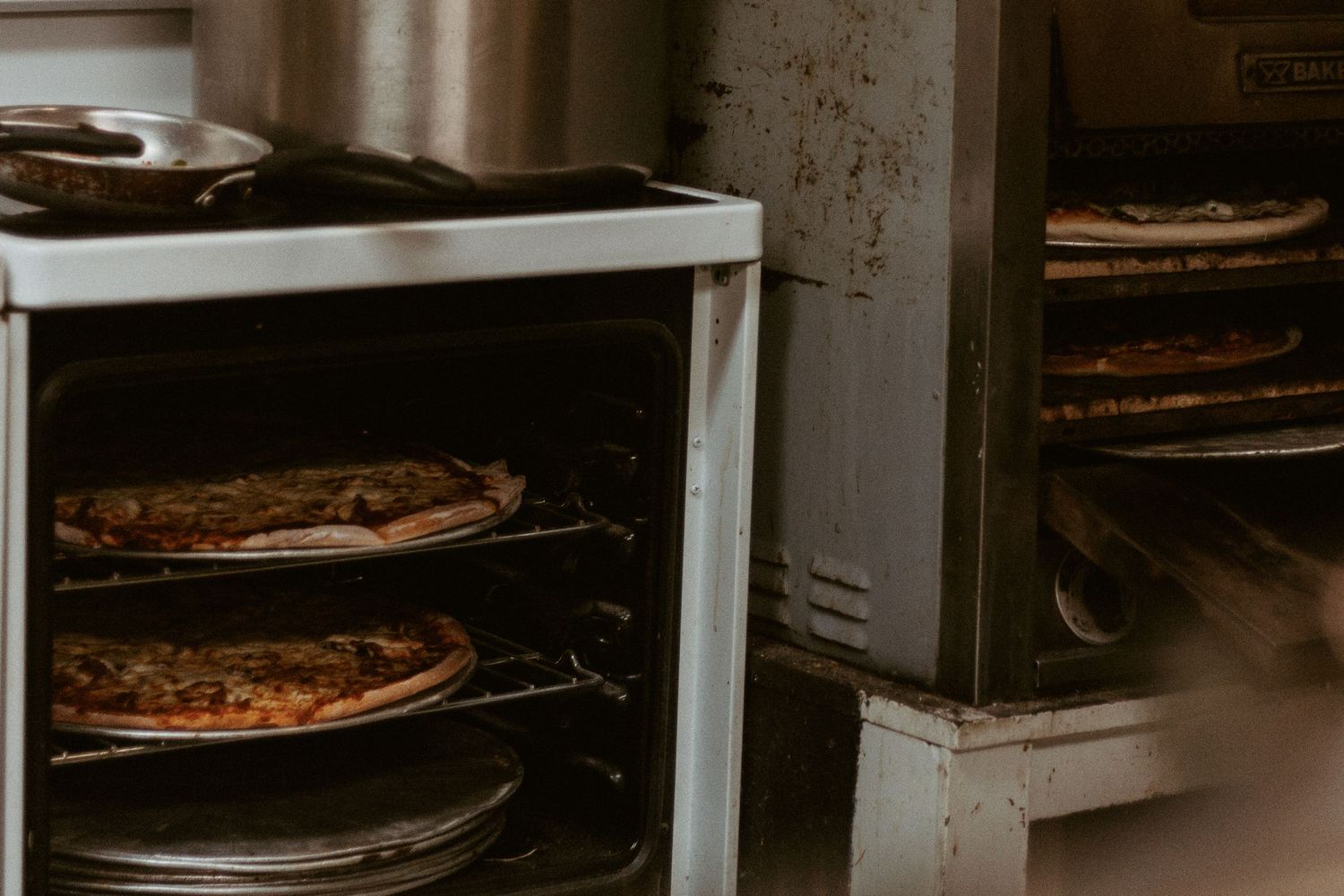 Multiple pizzas cooking on racks in a commercial pizza oven.