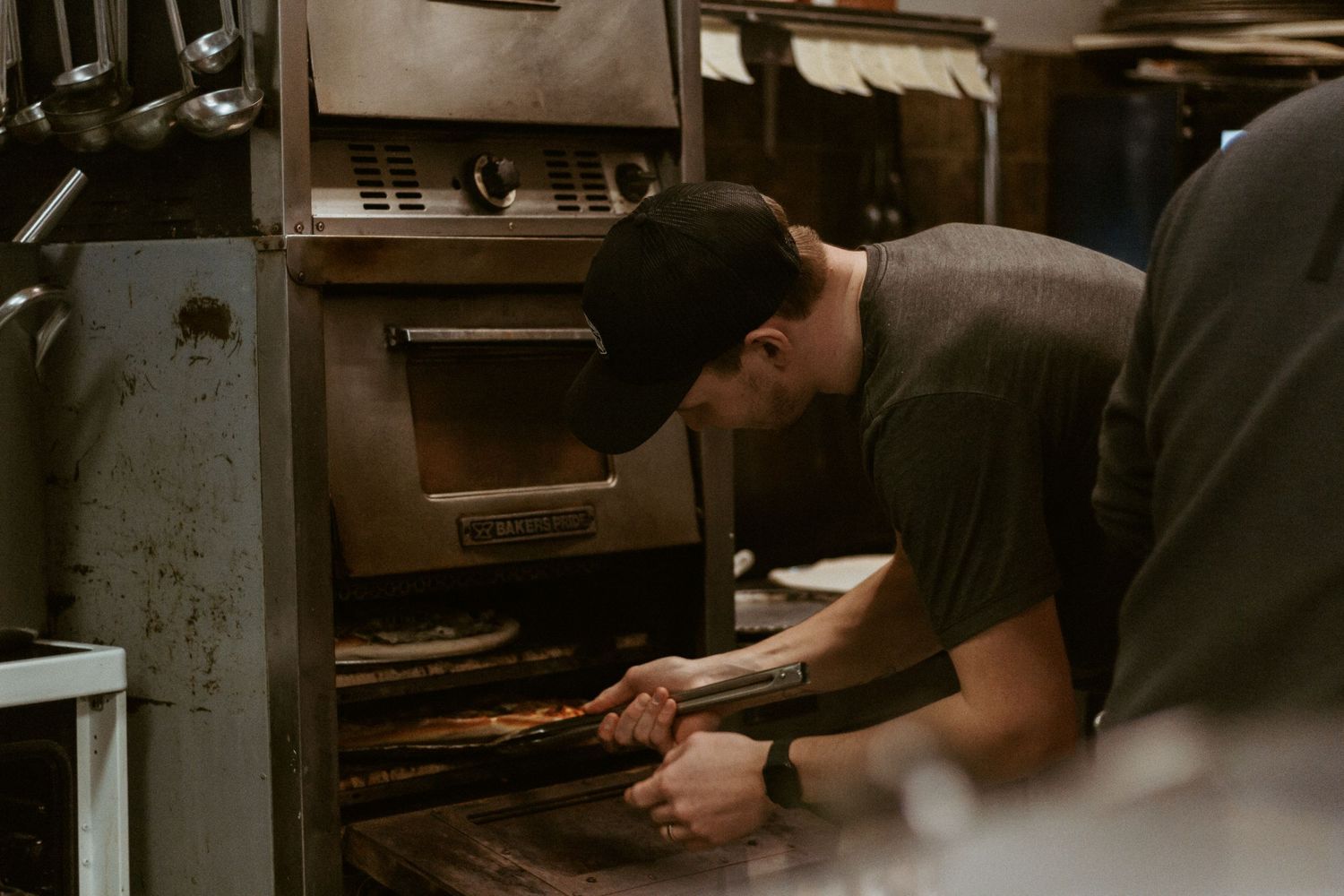 Pizza maker checking food in commercial kitchen oven.