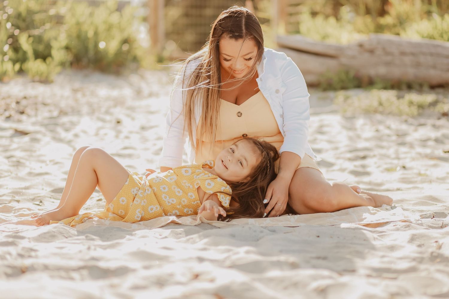 Mother and baby playing together on white sandy beach in natural sunlight.