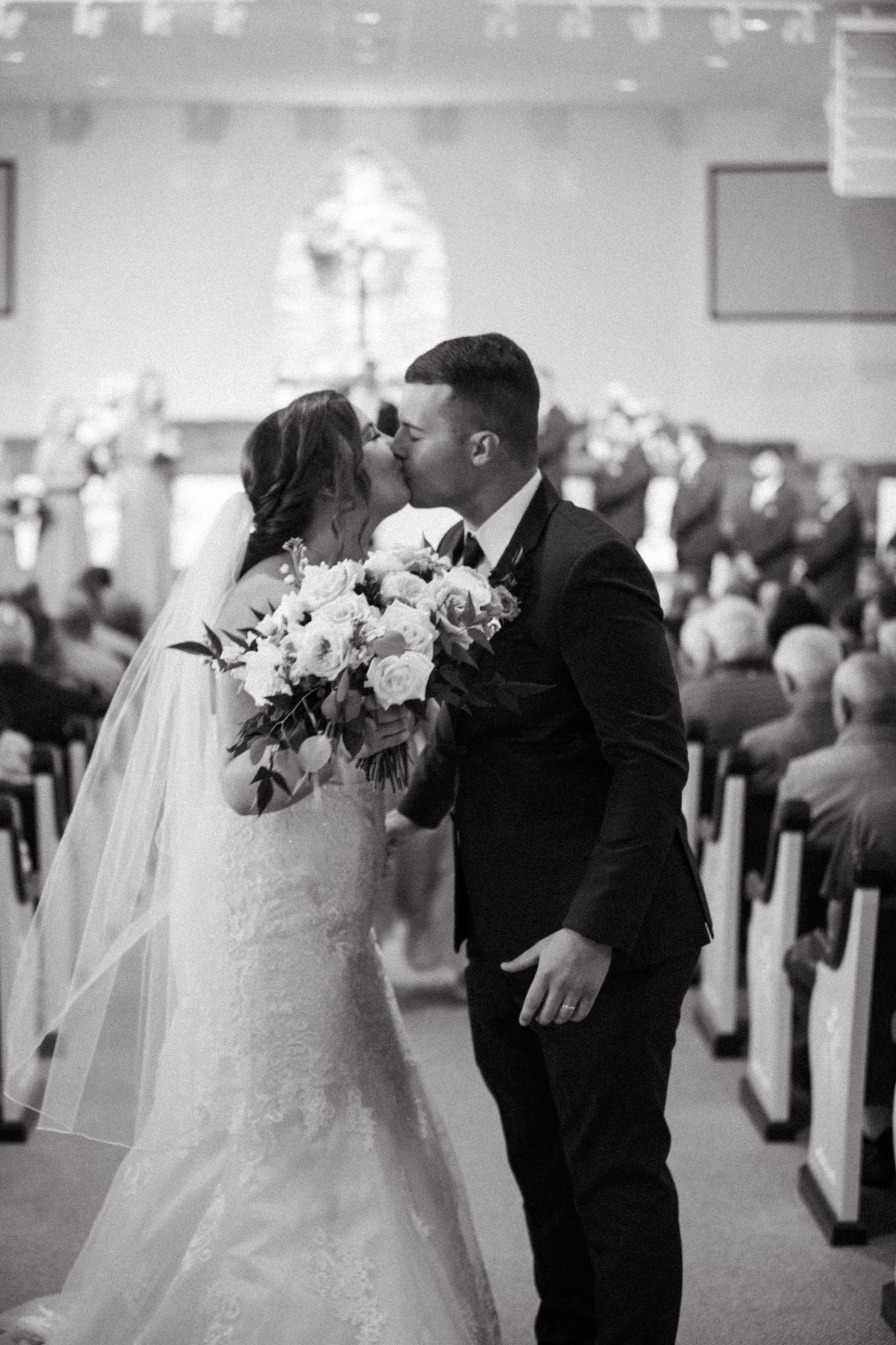 Wedding ceremony in a grand indoor venue with rows of guests seated in pews.
