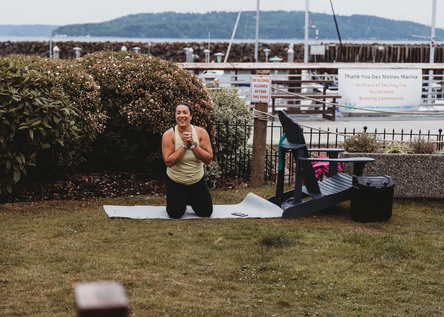 Person doing yoga or exercise on mat near waterfront with boats in background.