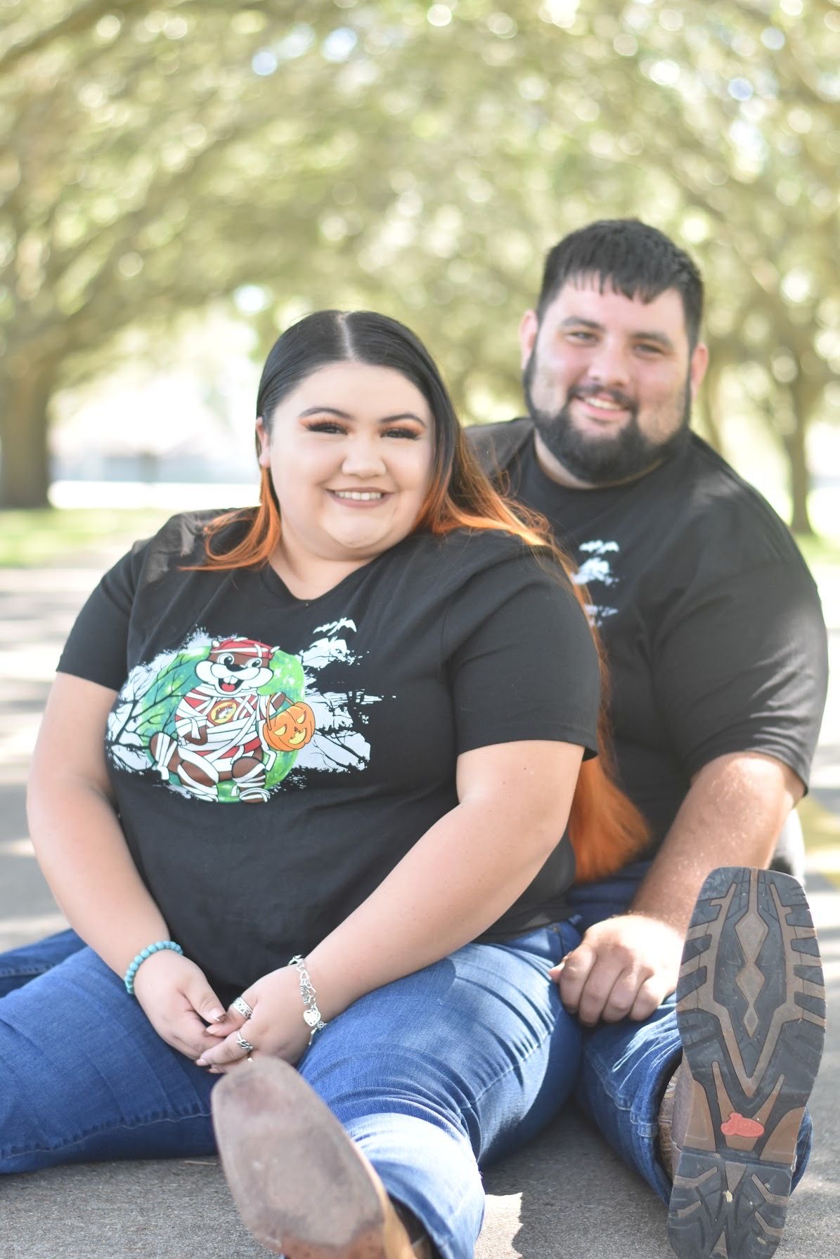 Couple sitting together wearing matching graphic t-shirts outdoors.
