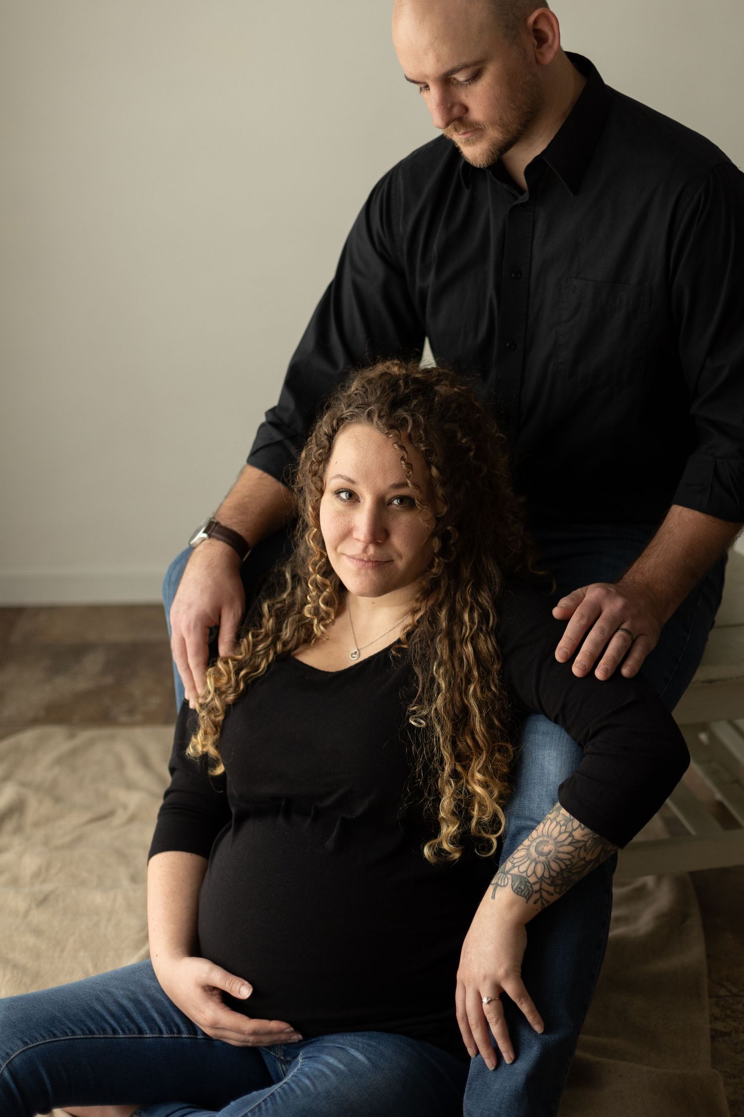 A pregnant wife cradles her first baby-bump while leaning on her husband.