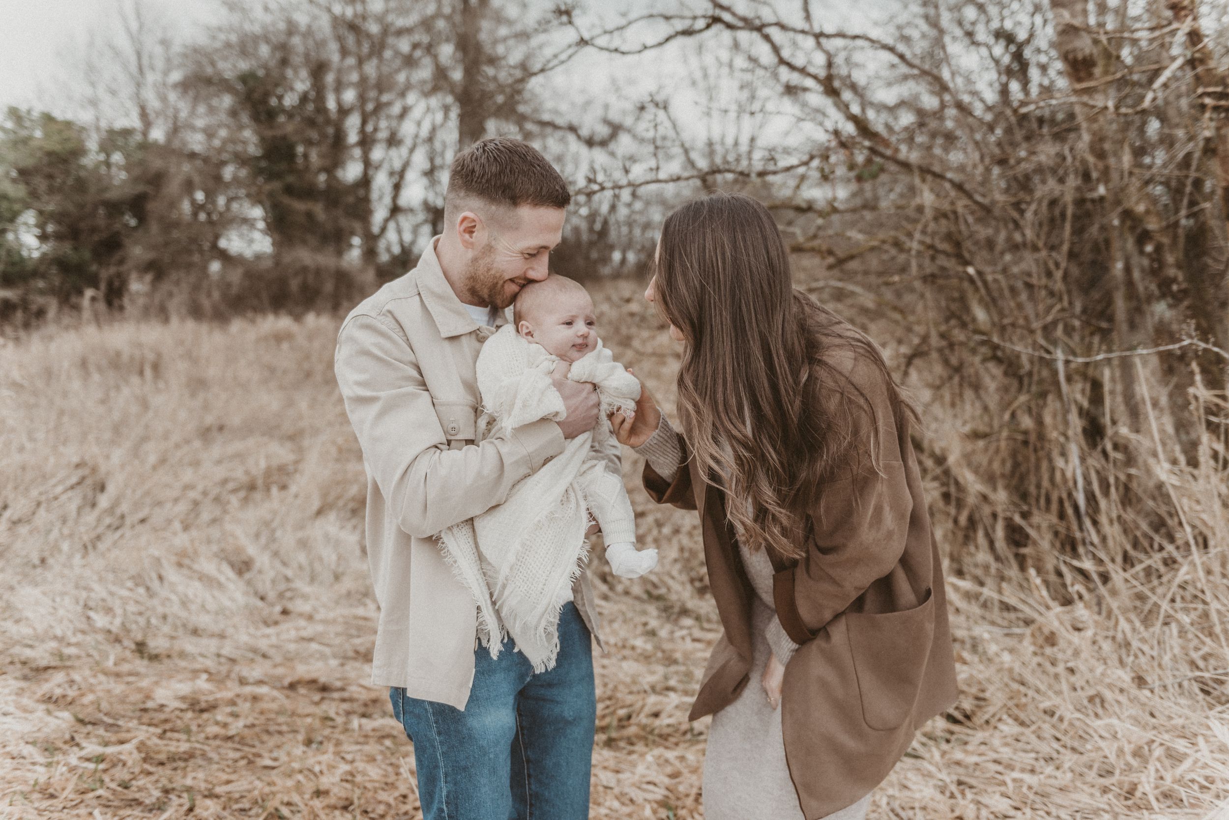 A precious family moment outdoors with parents cradling their baby against a natural backdrop.